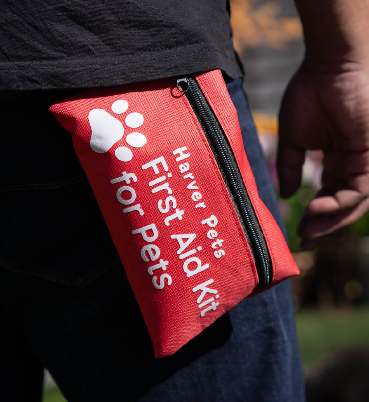 Red 'Harver Pets First Aid Kit' pouch clipped onto waistband of a person outdoors.